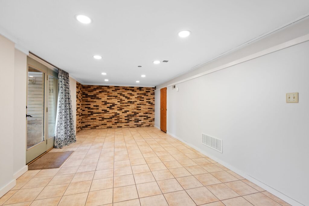 Bright basement with brick accent wall and durable epoxy tile flooring in Charleston home